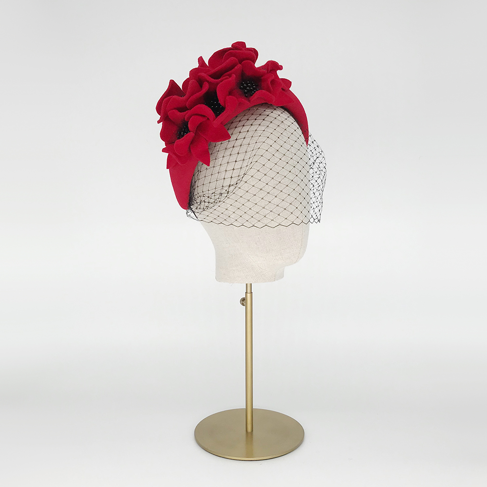 A red felt headband decorated with matching felt leaves and poppies which have been beaded in the center ith black beads. it is displayed on a white mannequin head on a gold stand. . 